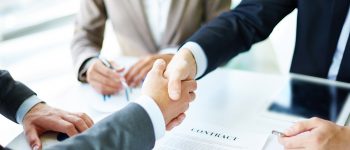 Image of business partners handshaking over business objects on workplace