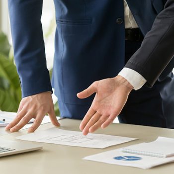 Businessman pointing on apartments drawings lying on desk during construction project presentation. Architect or realtor discussing house plan with client. Internal space planning. Close up image